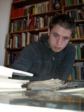 Chris in a library, gazing at a plie of books