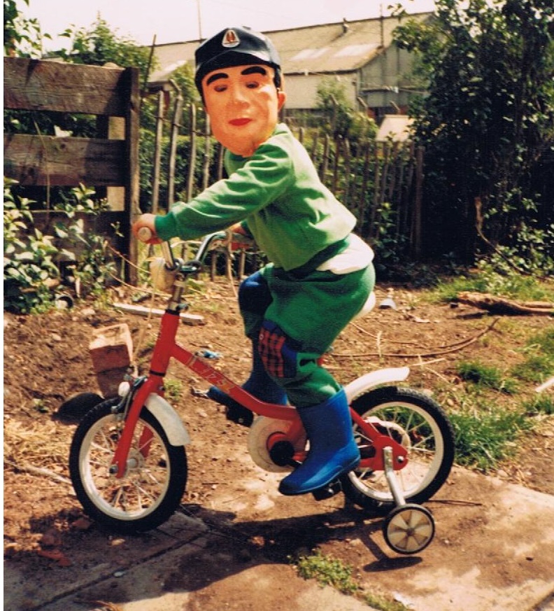 Chris aged about 5, riding his little bike with stabilisers and wearing his "false face" mask